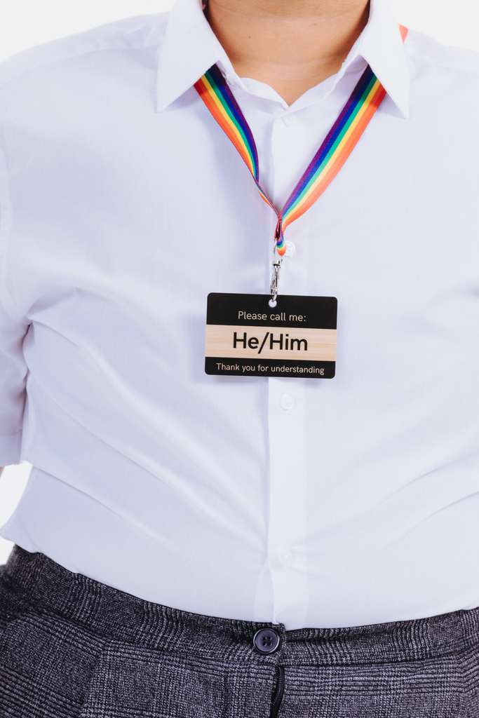 Person wearing a white shirt with a rainbow lanyard and a card tag indicating pronouns.