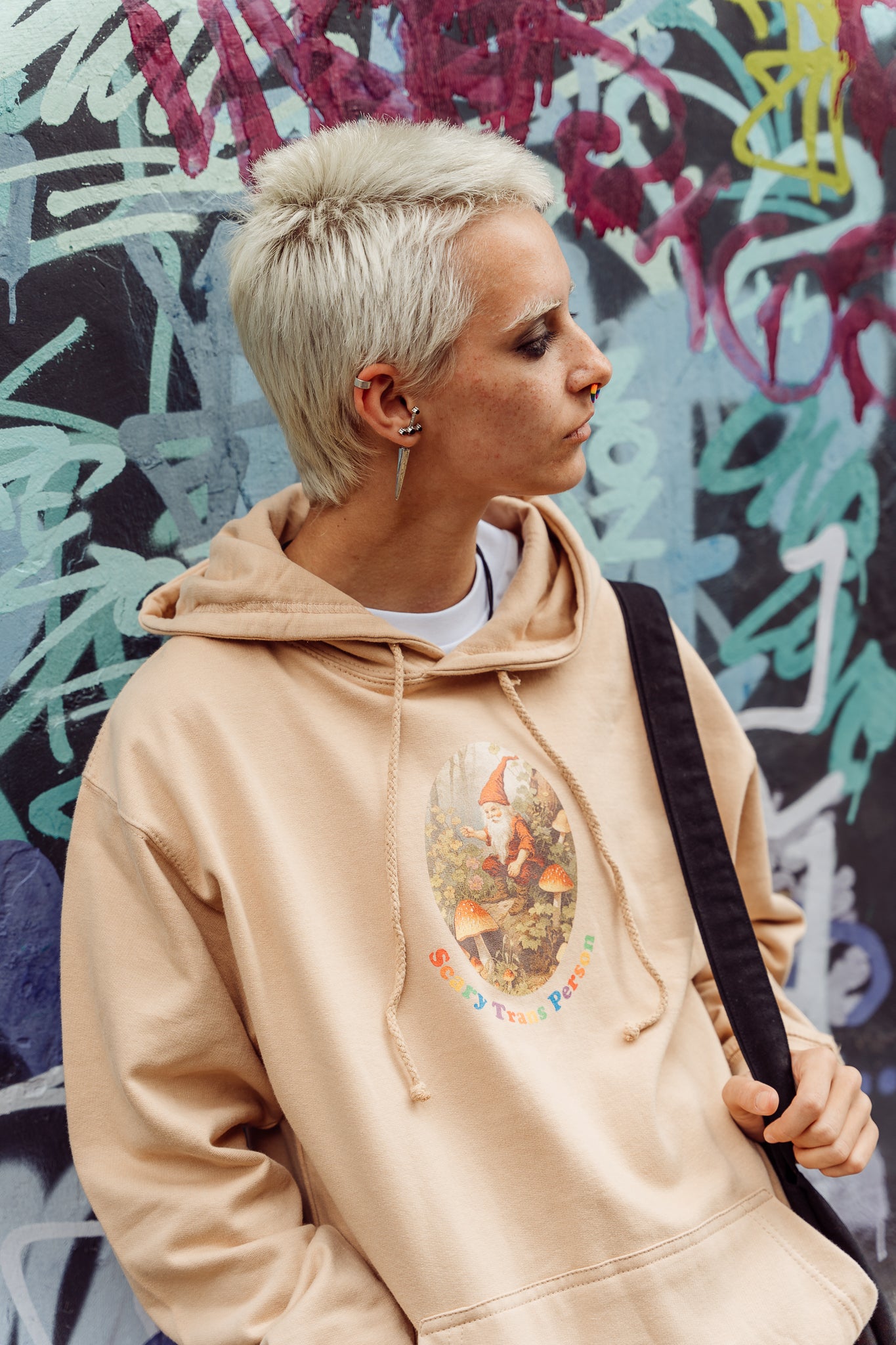 Person wearing a beige hoodie with a graphic of a woodland gnome featuring the text "scary trans person".