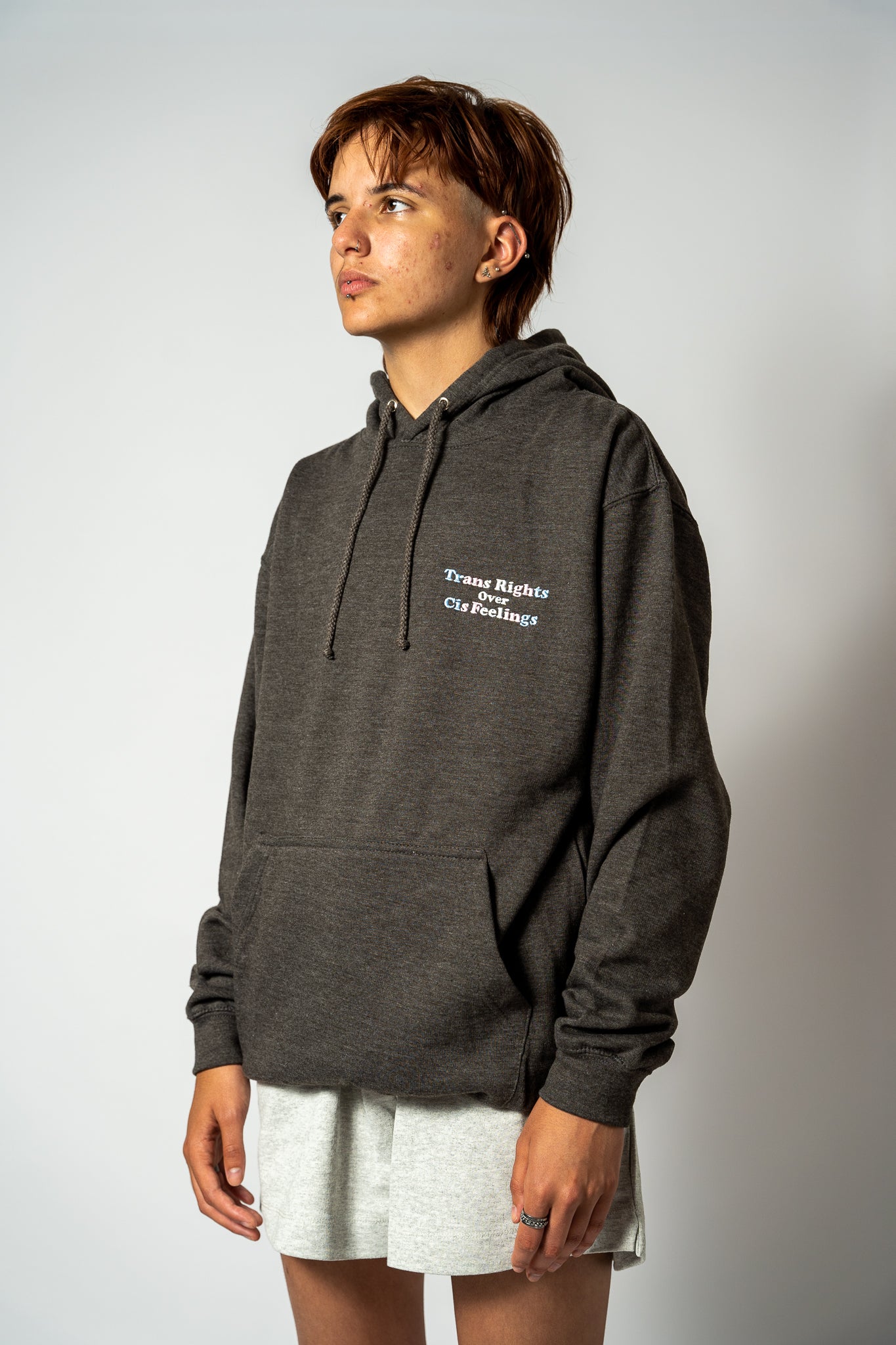 Person wearing a dark gray hoodie with "Trans Rights Over Cis Feelings" text on a plain background