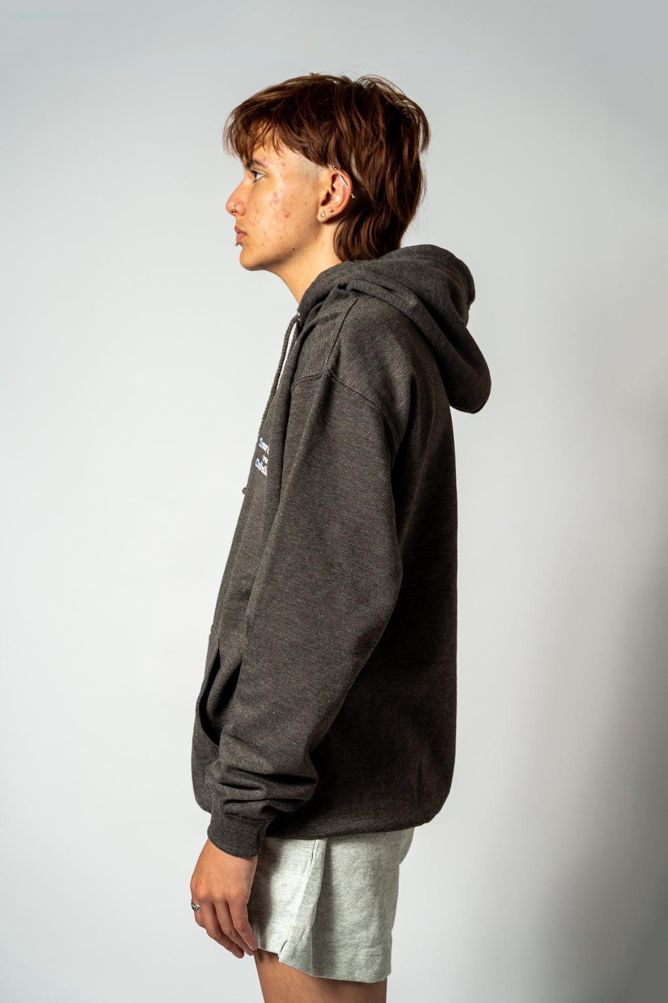 Person wearing a dark gray hoodie and light-colored shorts on a plain background