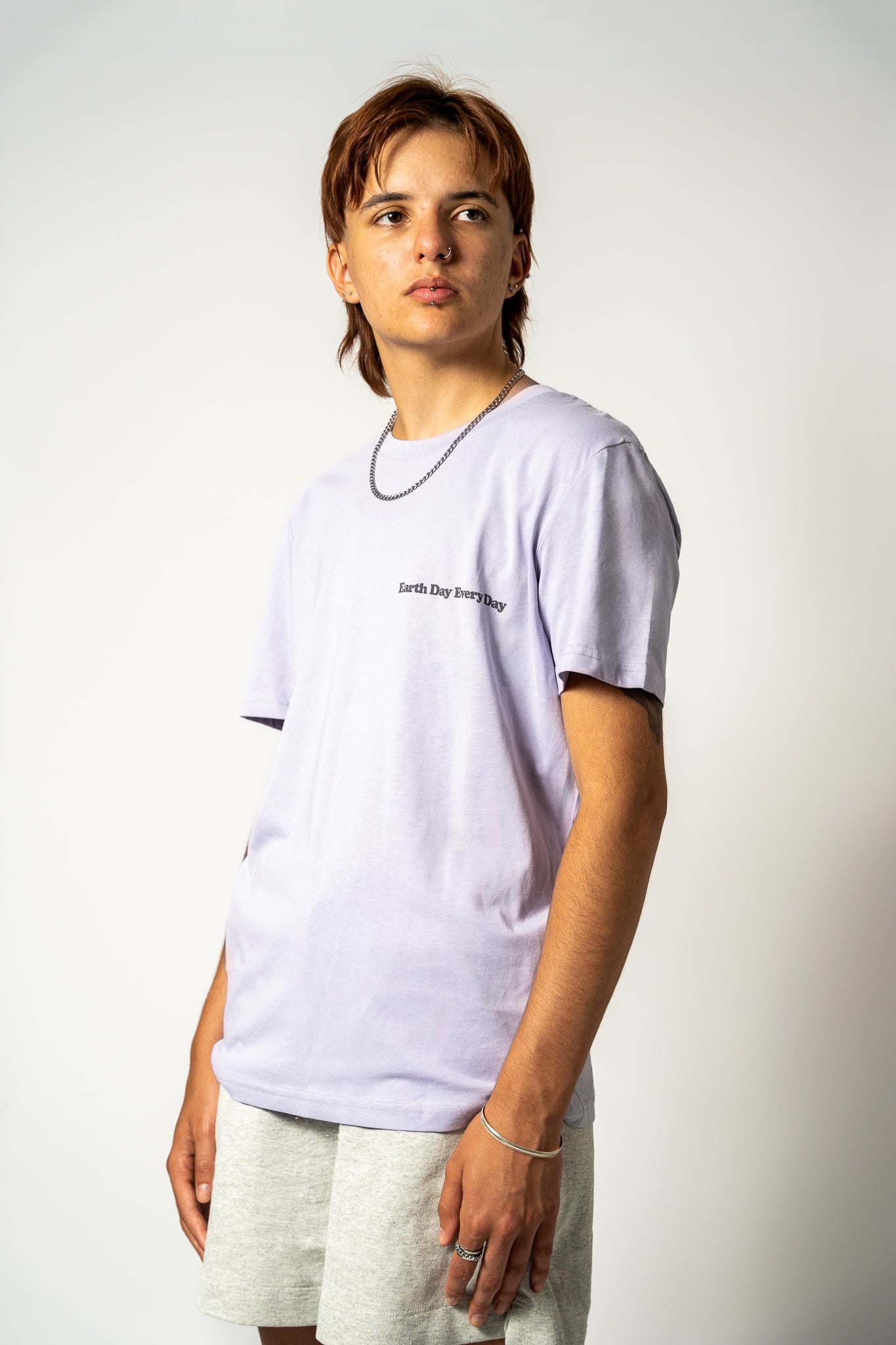 Person wearing a light purple t-shirt with 'Earth Day Every Day' text on a plain background